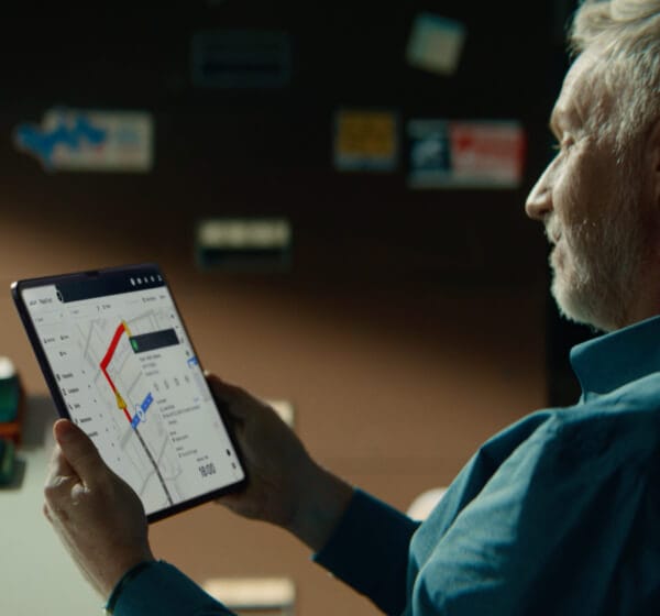 Älterer Mann hält ein Tablet, das Fahrzeugflottenanalysen zeigt.