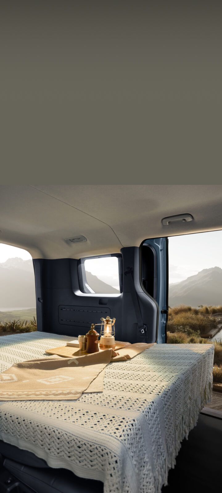 Innenraum des Kia PV5 Passenger mit flach umgeklappter Rücksitzbank und Blick auf eine malerische Landschaft.