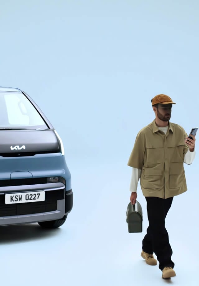 Hand hält ein Smartphone mit dem digitalen Schlüssel des Kia PV5 vor dem Fahrzeug